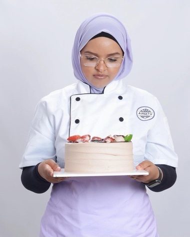Amaturahaman in her chef whites, holding a cake she baked