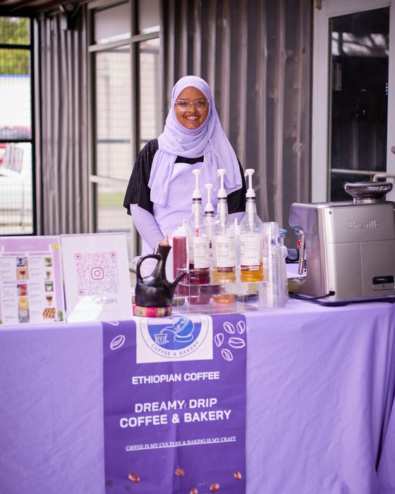 Amaturahaman at her Dreamy Drip stand, beneath a banner reading ‘Coffee is my culture and baking is my craft’